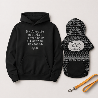 A black hoodie and matching black pet dog coat with white text and cat-face pattern, displayed on a light gray background with an orange leash.