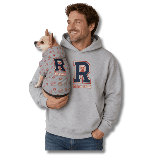 A man holding a small dog wearing a gray hoodie with a paw print and large letter 'R' graphic, while the man wears a matching gray hoodie with a large letter 'R' and the words 'Rescue Dad' on the front. The background is solid white.