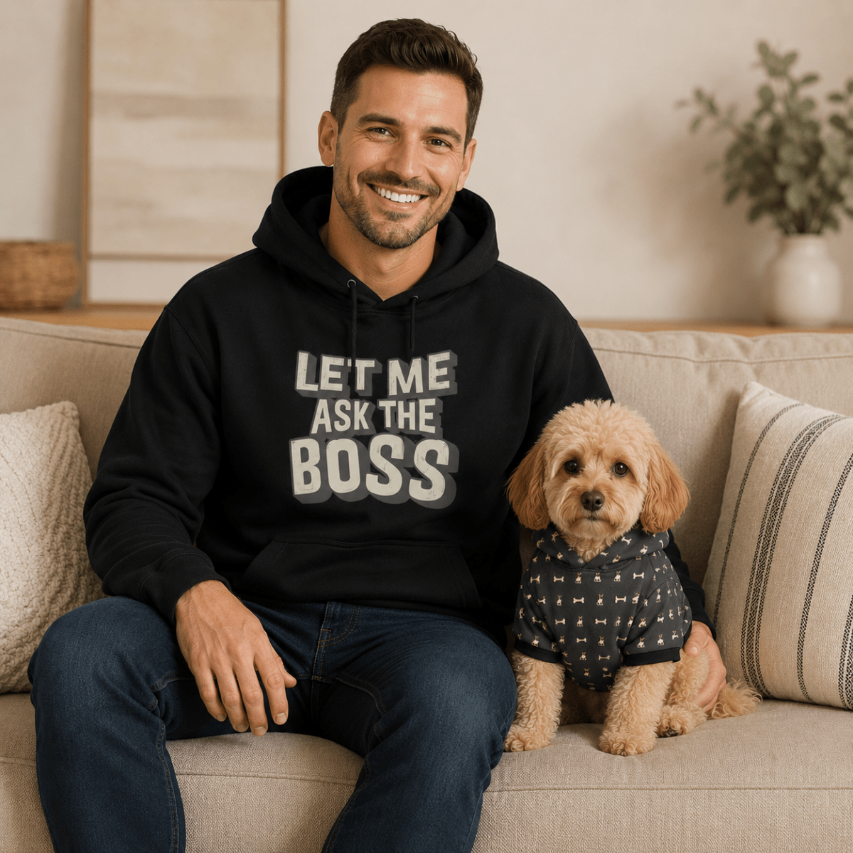 Man wearing a black hoodie with text sitting on a couch with a dog.