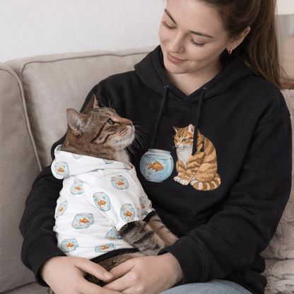Woman wearing a black hoodie with a cat design, sitting on a couch with a cat in her lap.