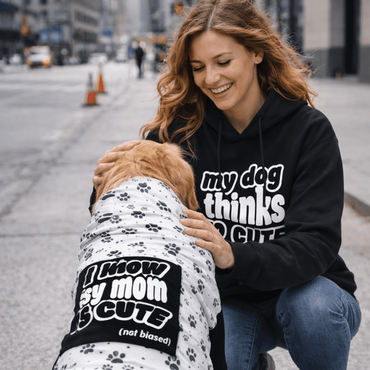 Woman in a black hoodie with text kneeling next to a dog wearing a matching outfit on a city street.