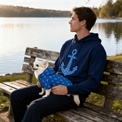 Man sitting on a bench by a lake with a small dog in his lap, both wearing blue outfits.