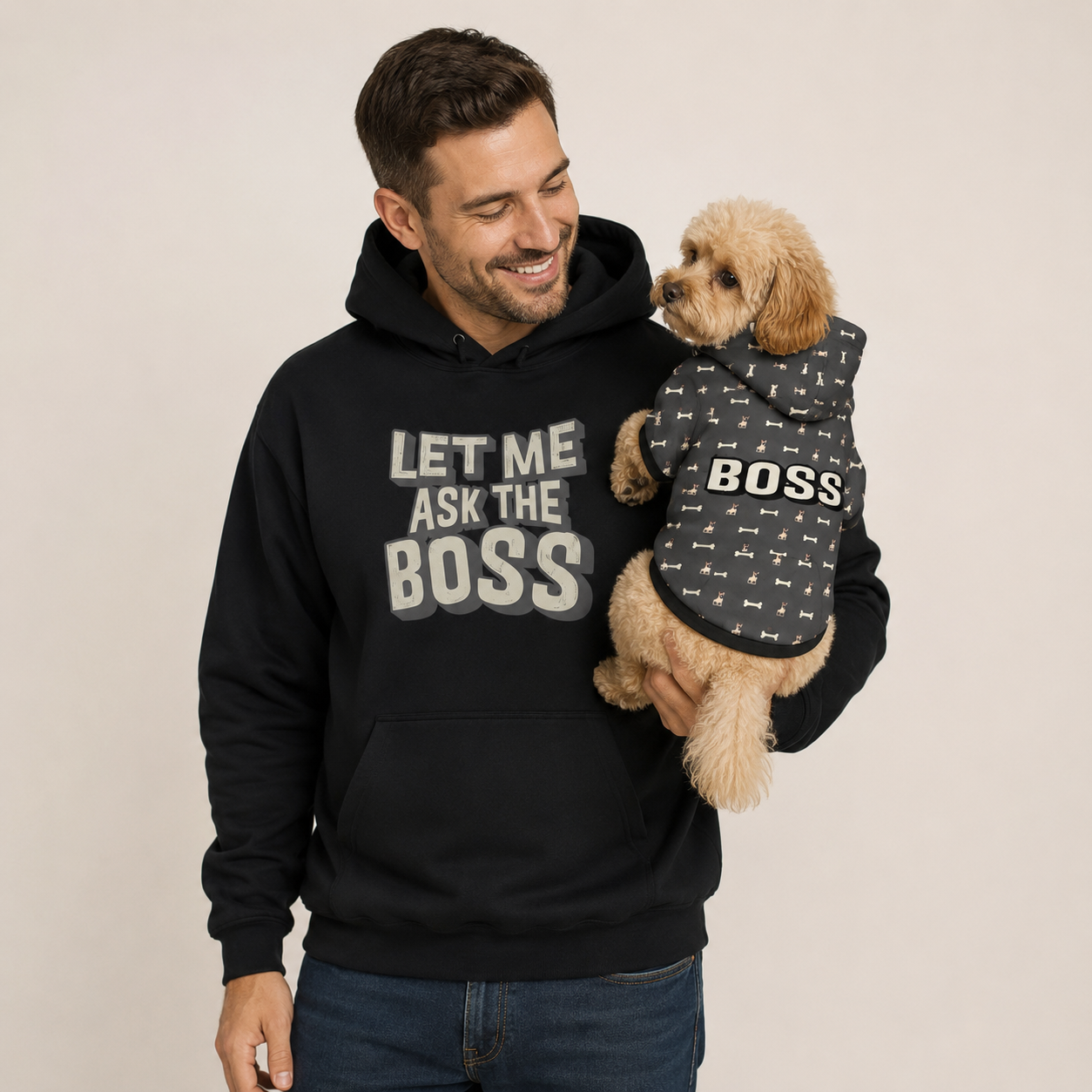 Man wearing a black hoodie with 'Let Me Ask The Boss' text, holding a dog in a matching 'BOSS' hoodie.