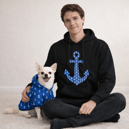 Man wearing a black hoodie with a blue anchor design, sitting next to a dog in a matching blue outfit.