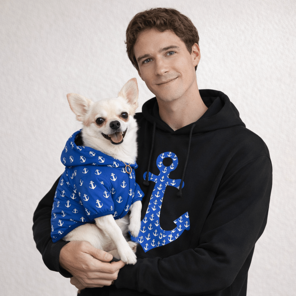 Man holding a dog wearing a blue hoodie with anchor patterns on a light gray background