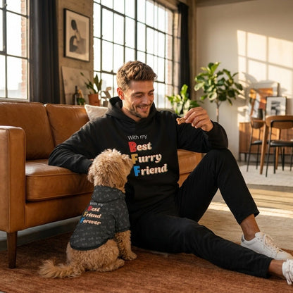 Man sitting on the floor with a dog wearing matching sweatshirts in a living room.